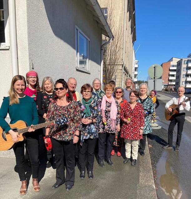 Musiikiryhmä Kohti Kaustisen kansanmusiikkijuhlia poseeraa kadulla parin kitaran kanssa kauniina kevätpäivänä.
